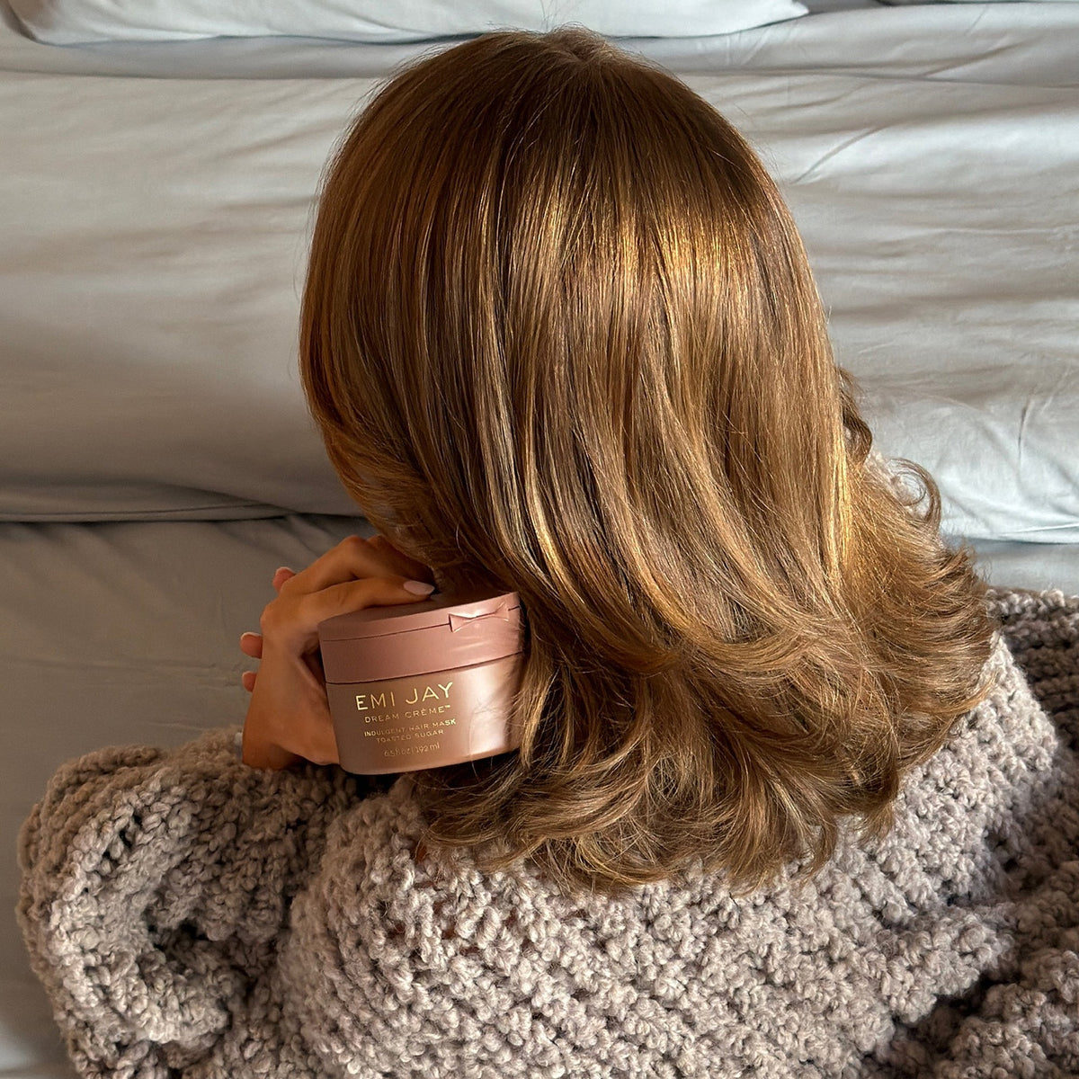 model holding Dream Crème in Toasted Sugar tub next to hair