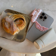 Angel Hold Plushie Sticker on phone with angel hold styling cream, sweetheart clip, and pastry on table