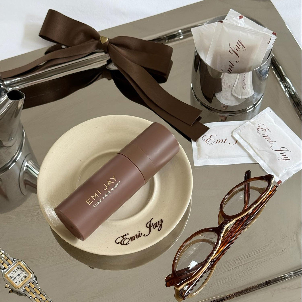 Aura Hair + Body Mist in Toasted Sugar with Bow Barrette in Toasted Sugar on tray with Emi Jay sugar packets, glasses, watch, plate, and kettle.