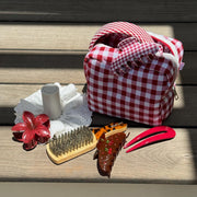 Gingham Pouch in Cherry Kiss on wood with assorted hair care, accessories, and styling tools