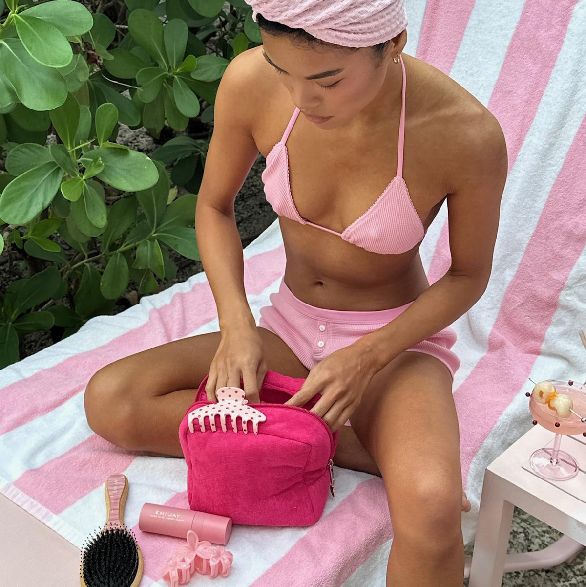 model wearing hair towel looking inside Terry Pouch in Lychee Baby next to aura hair + body mist in lychee baby, hair clips, and brush
