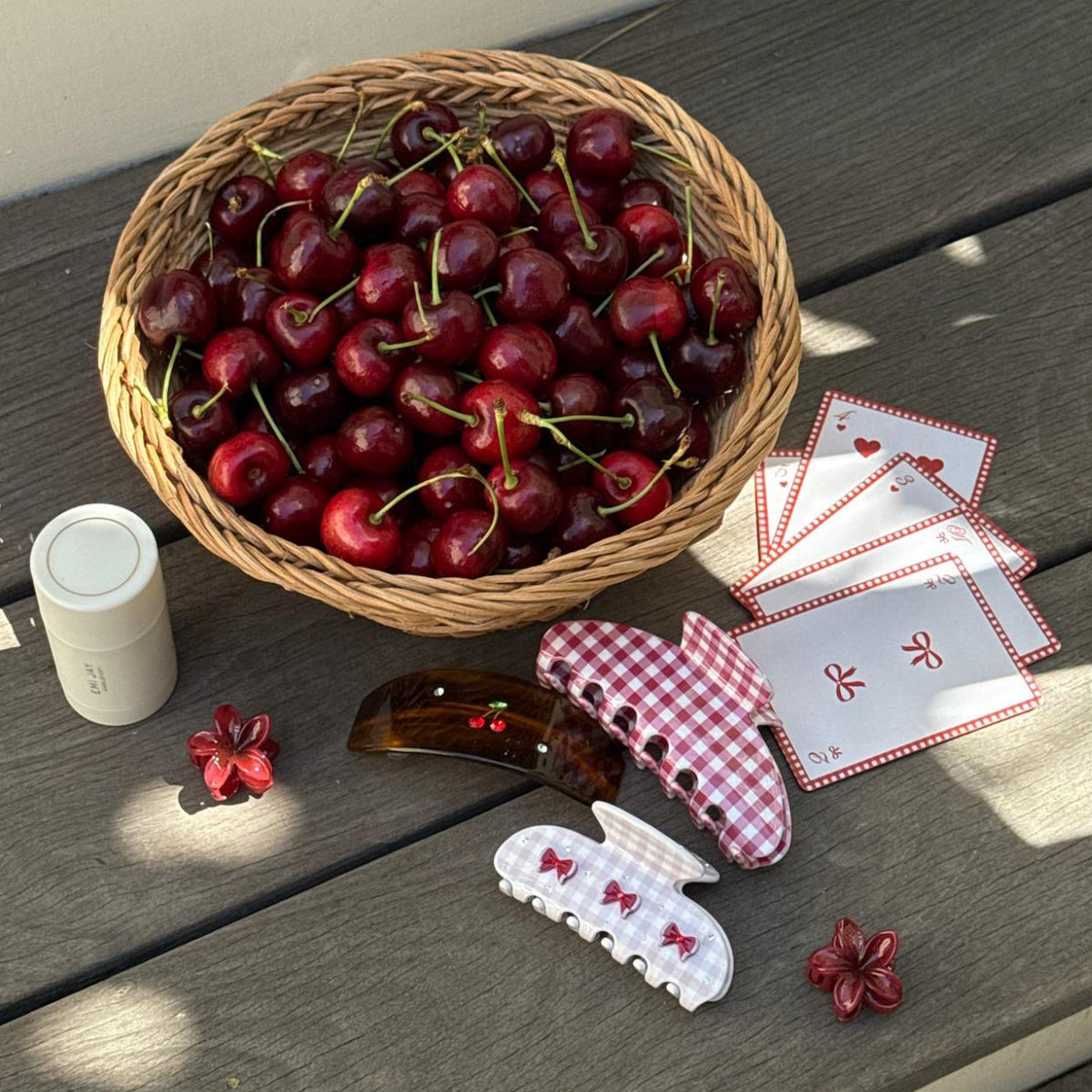assorted emi jay hair accessories and angelstick next to a basket of cherries and playing cards