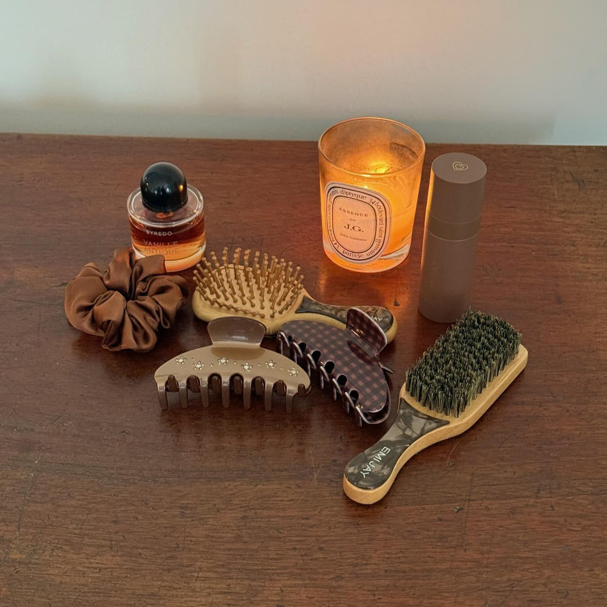 Assorted Emi Jay hair accessories and styling tools with candle and Aura Hair + Body Mist in Toasted Sugar.