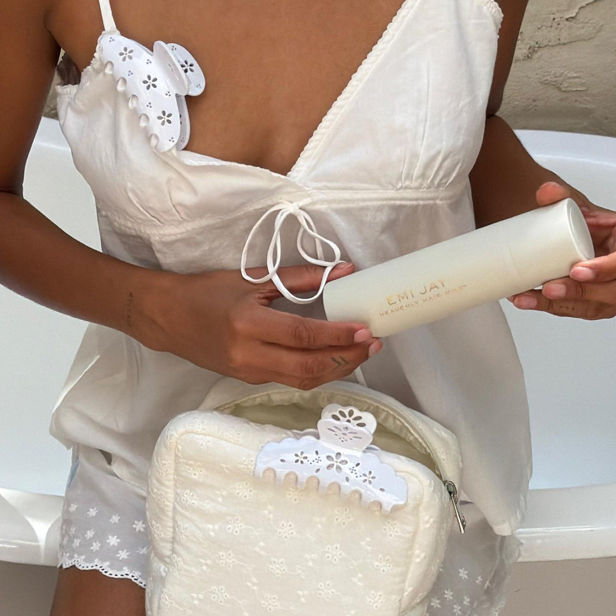model wearing Lil Effing Clip in Blanc Petal Eyelet clipped to strap while holding heavenly hair milk above pouch with big effing clip