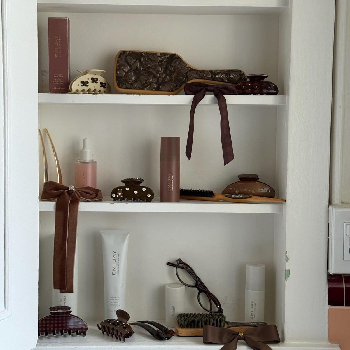 Assorted Emi Jay hair care, accessories, and styling tools on shelves in cabinet.