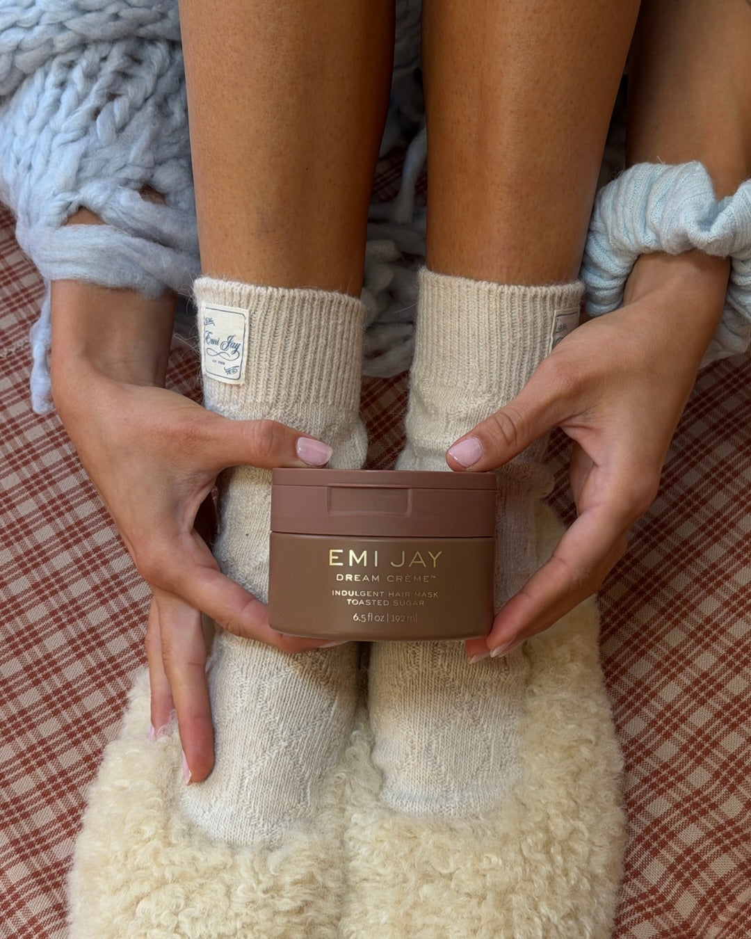 Model in cozy knit socks holding EMI JAY Dream Crème in Toasted Sugar